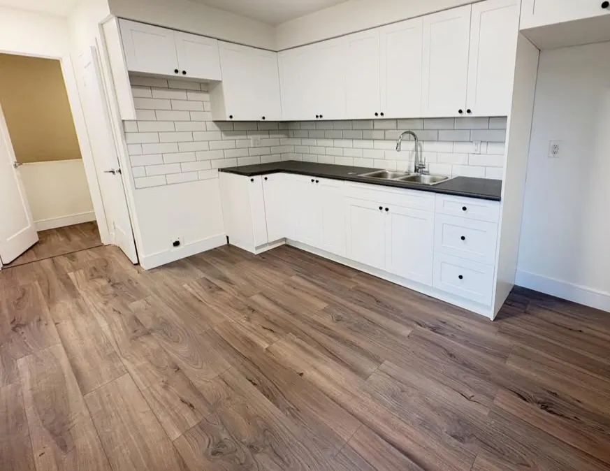 Renovated apartment kitchen with white shaker cabinets, white subway-tile backsplash, dark countertop and wood-look laminate floor